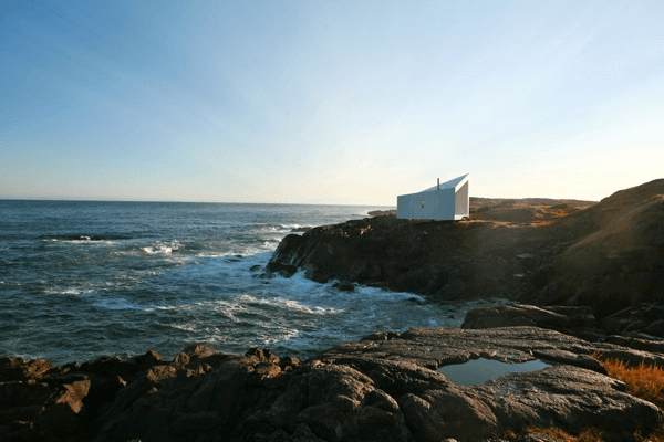a small white building sitting on top of a rocky shore